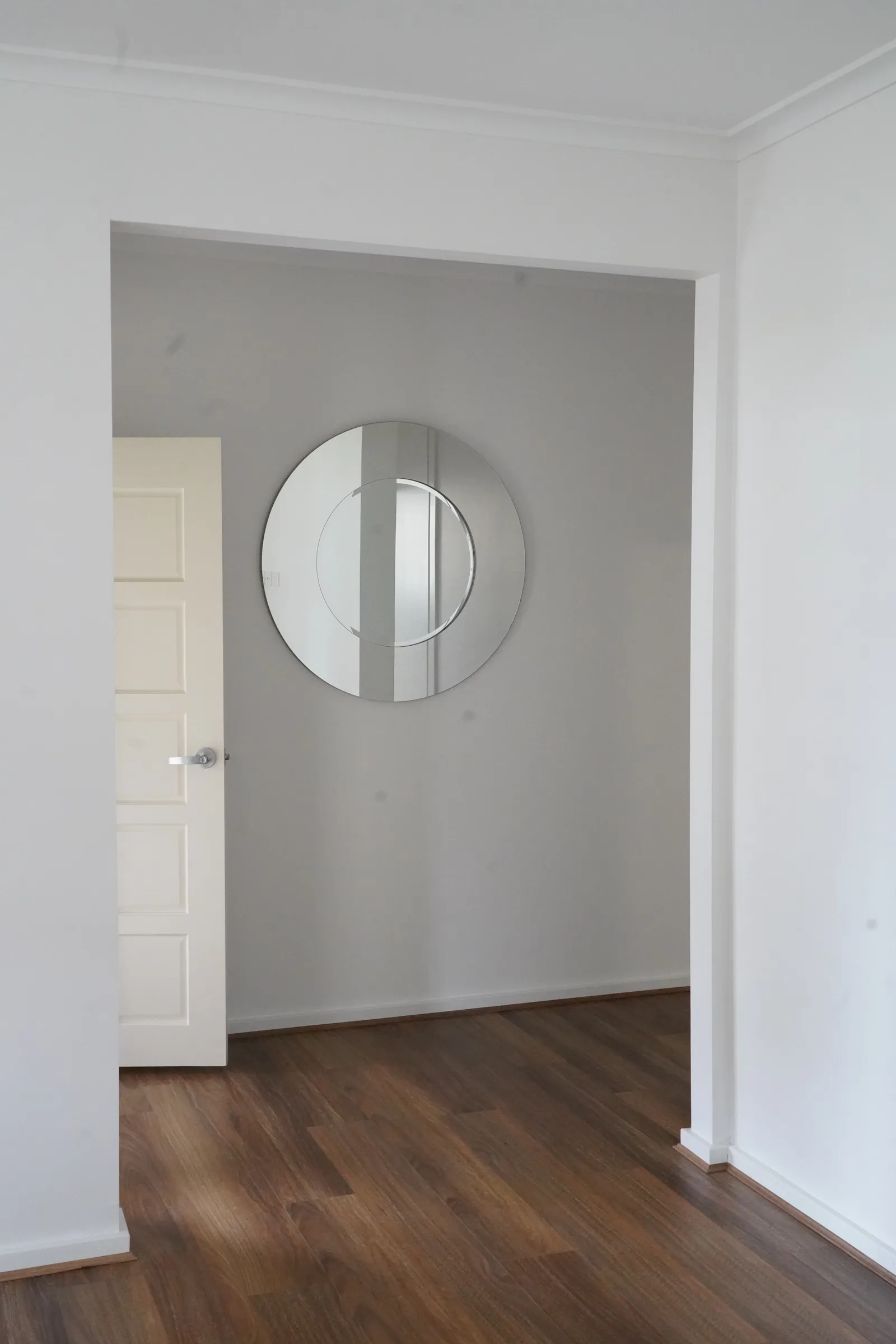 Repainted hallway with new timber-look flooring and a round mirror