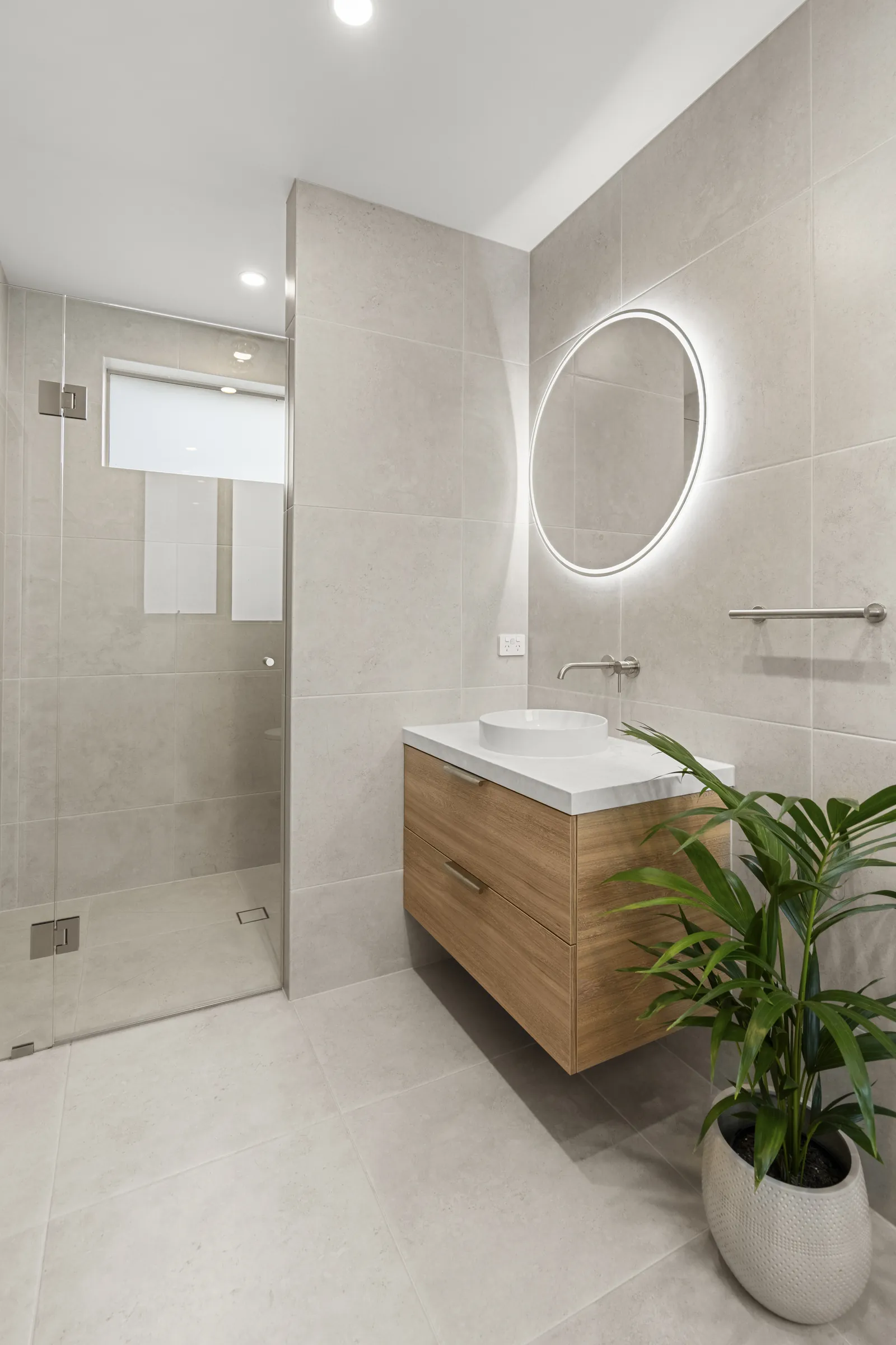 Walk-in shower with a frameless glass screen beside a floating vanity
