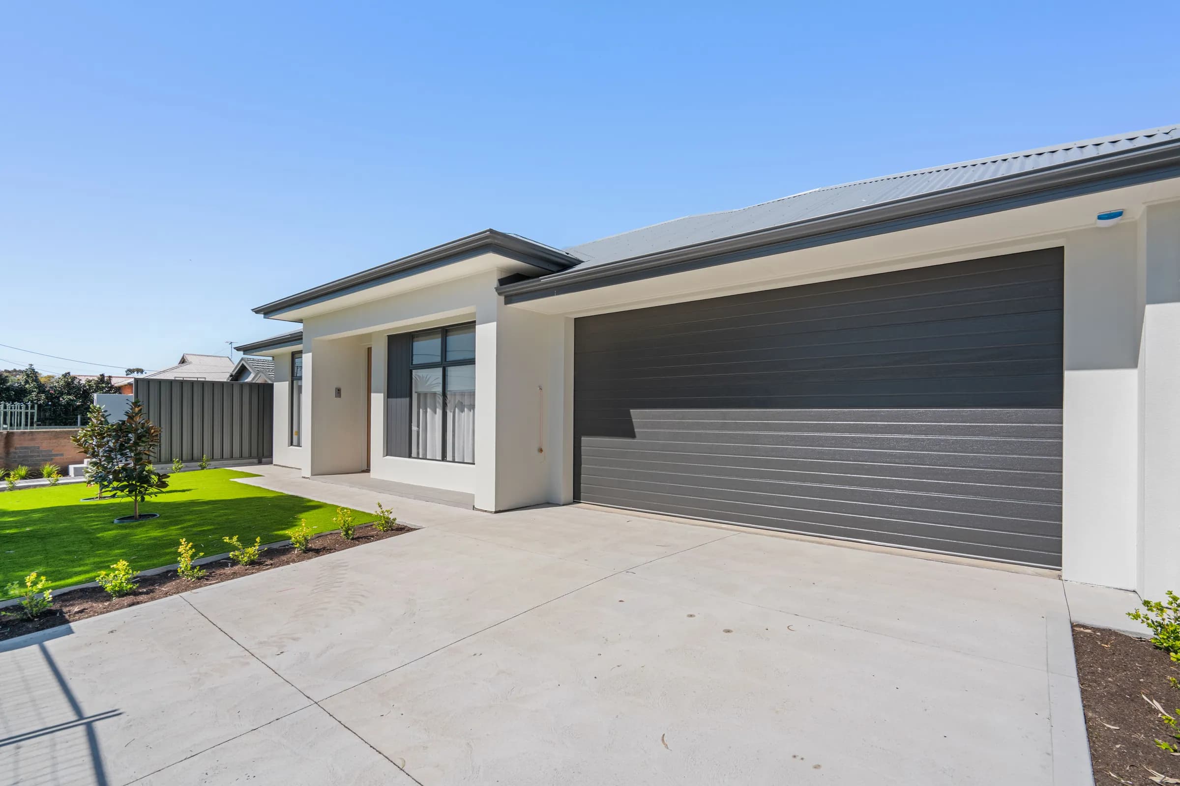Front of a completed single-storey home in Queenstown with a dark garage door and landscaped front yard