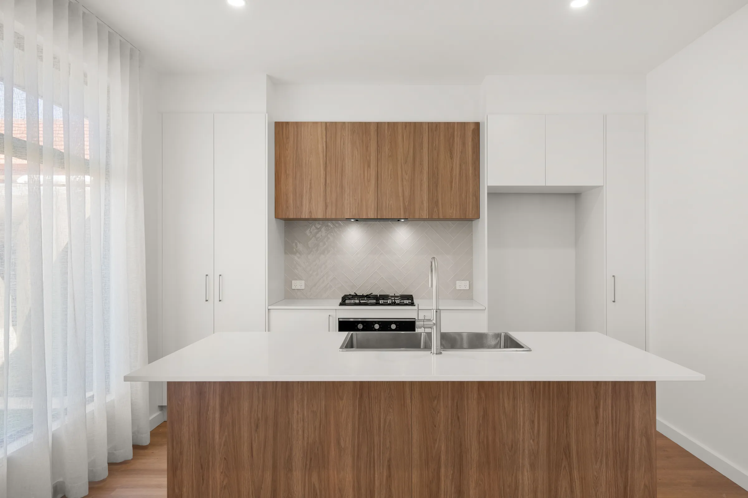 Open-plan kitchen with a timber-look island, white benchtop and herringbone tiled splashback