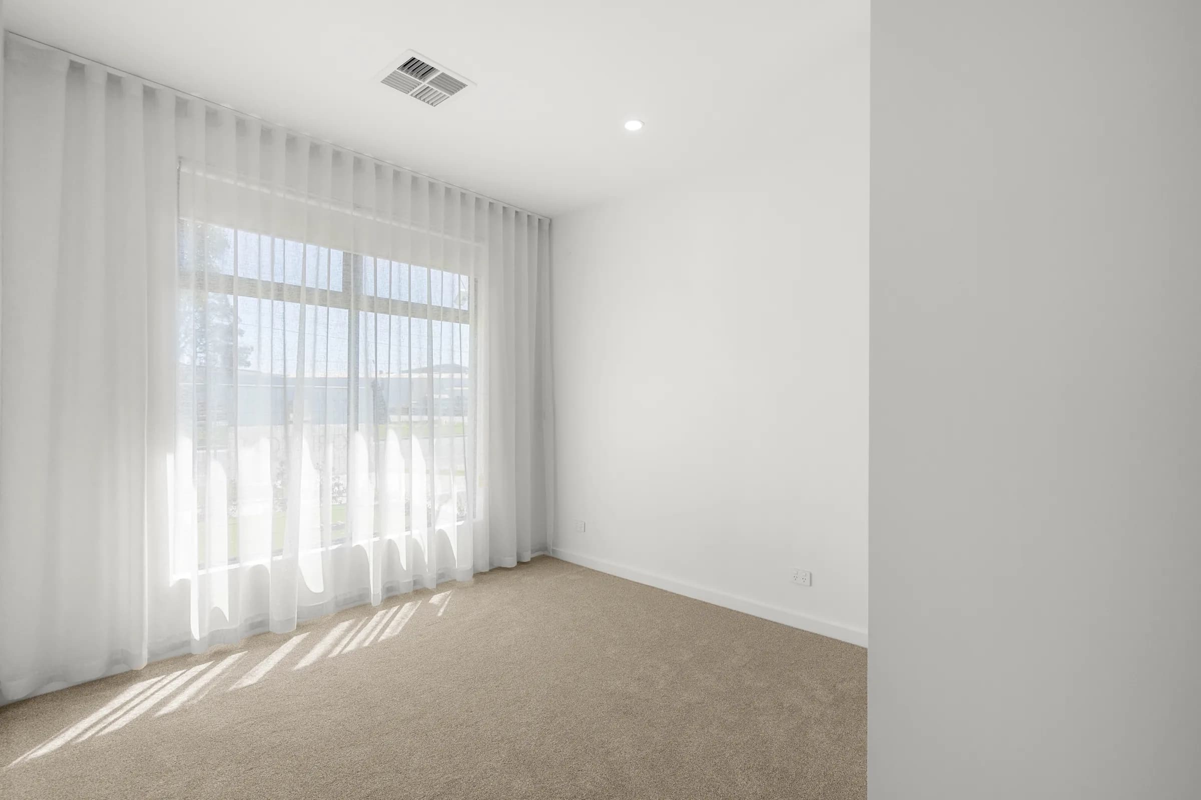 Bedroom with carpet, sheer curtains and a large window